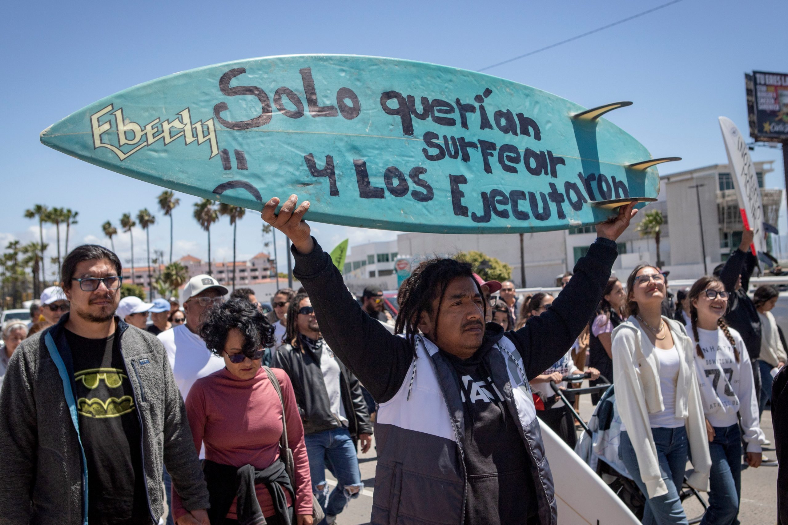 Un manifestante en Ensenada con una tabla de surf que dice: 'Solo querían surfear y los ejecutaron'